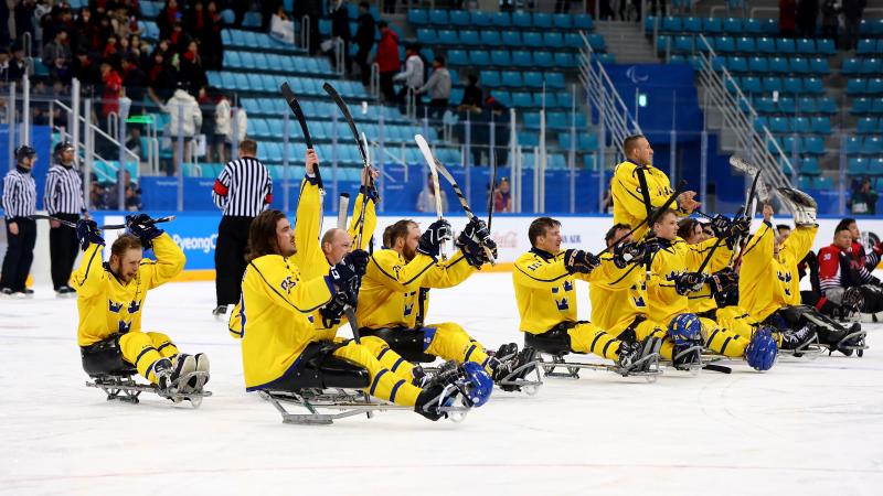 the Sweden Para ice hockey team raise their sticks in celebration on the ice