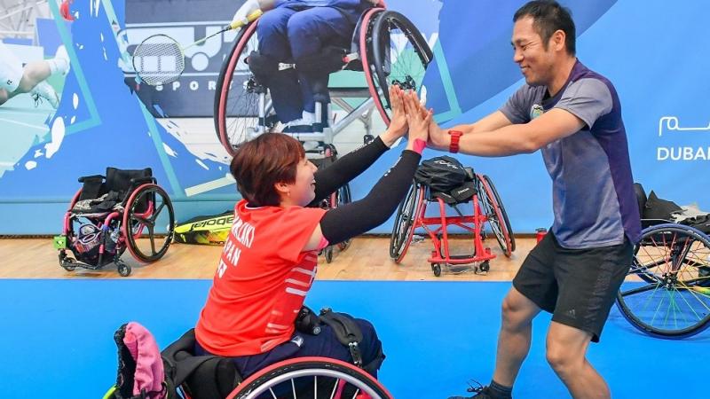 female Para badminton player Yuma Yamazaki sits in a wheelchair and high fives a standing man