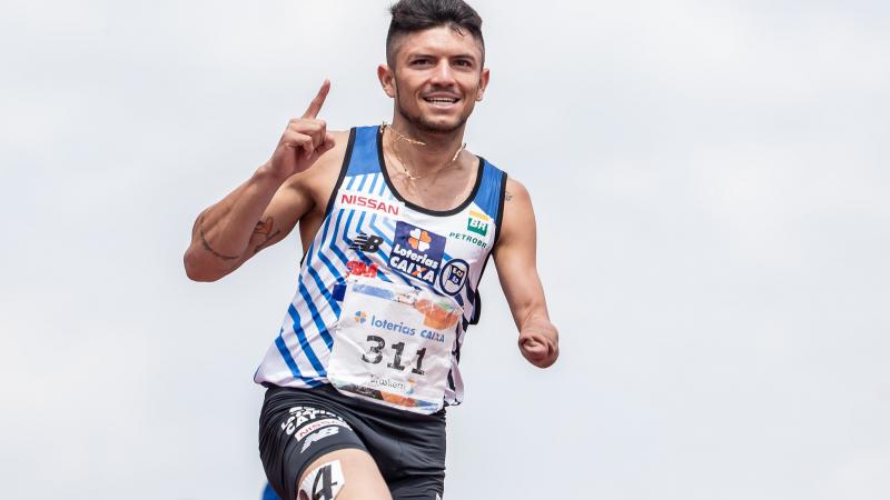 male Para athlete Petrucio Ferreira raises his finger as he crosses the finish line 