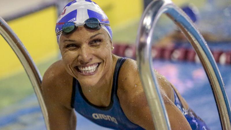 Female Para swimmer Maria Carolina Gomes smiles in the pool while leaning on the steps