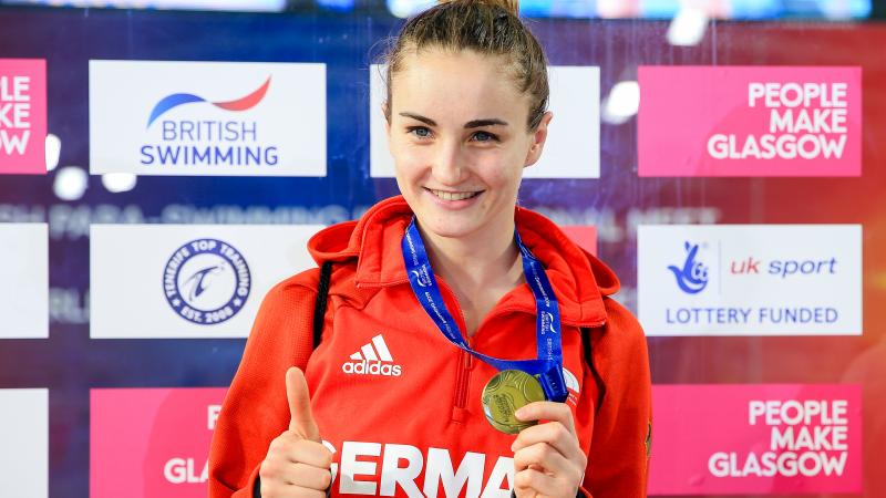 female Para swimmer Elena Krawzow gives a thumbs up and holds up her gold medal 