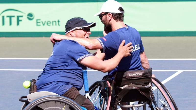 two male wheelchair tennis players from Israel hug on a hard court 