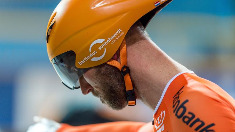 Dutch cyclist Vincent Ter Schure looking down while wearing a competition helmet and orange gear