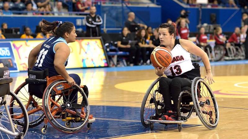Canadian wheelchair basketball player holds the ball as an Argentinian defender tries to prevent her from scoring