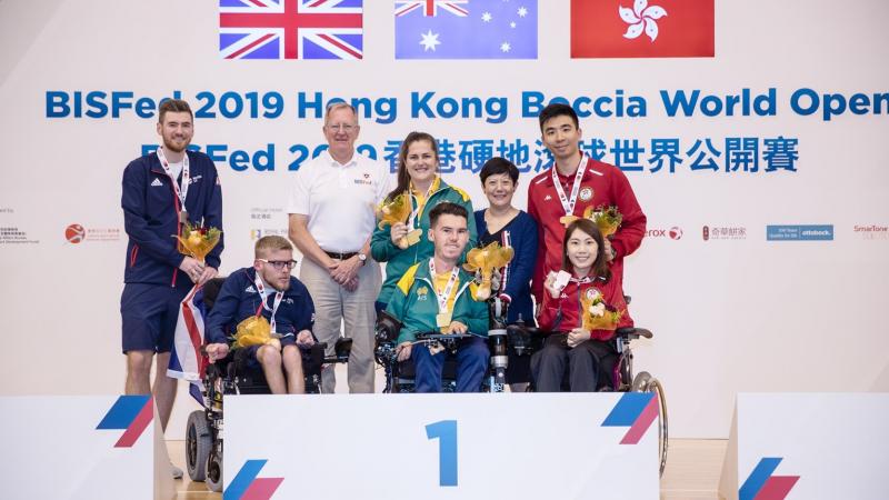 Podium photo with three boccia players and their assistants posing for a photo