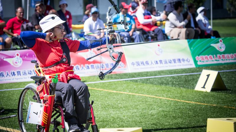 Chiense female archer in a wheelchair pulls back on her bow string