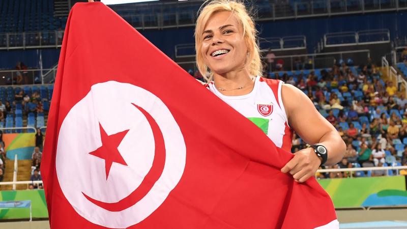 female Para athlete Raoua Tlili holds up the Turkish flag and smiles
