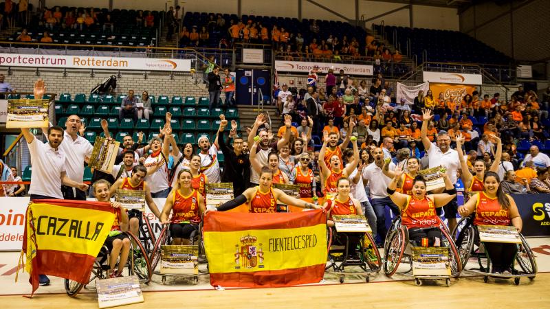 Spanish women's wheelchair basketball team and their staff celebrate as a group holding their hands up