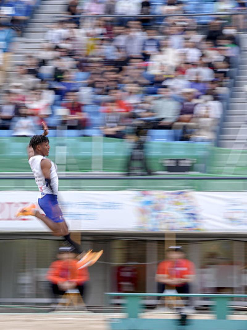 A man competing in the long jump in front of the crowd in a stadium