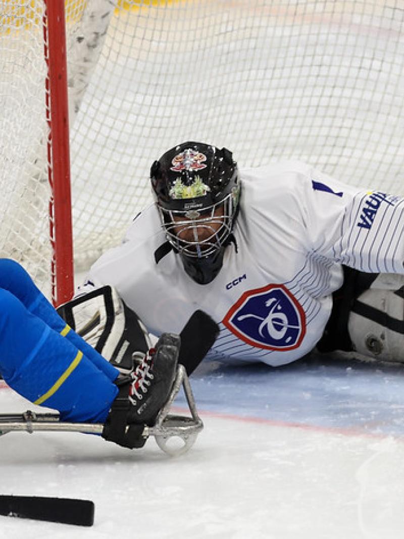 A male Para ice hockey player taking a shot in front of the goaltender