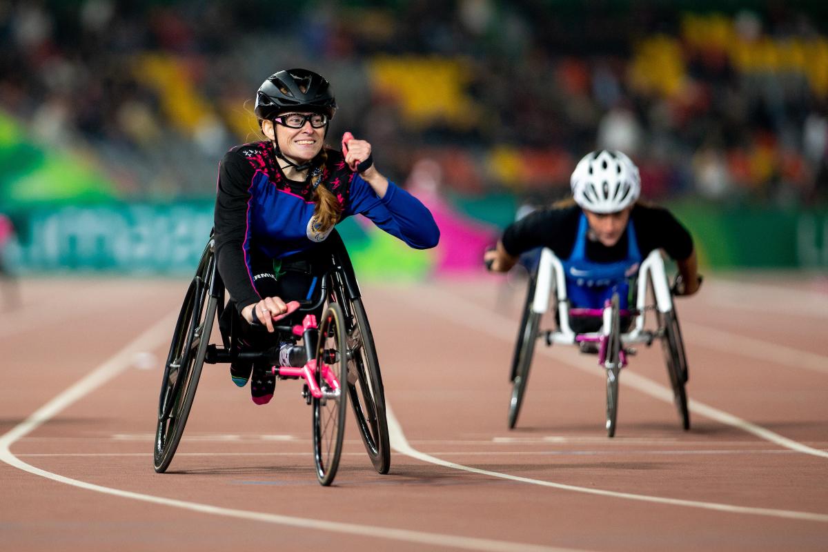 a female wheelchair racer clenches her fist as she crosses the finish line
