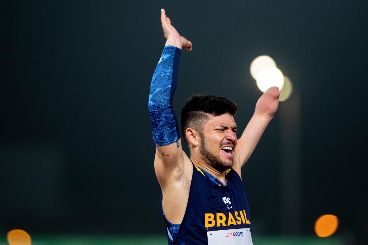 a male Para athlete throws his arms up in the air in celebration