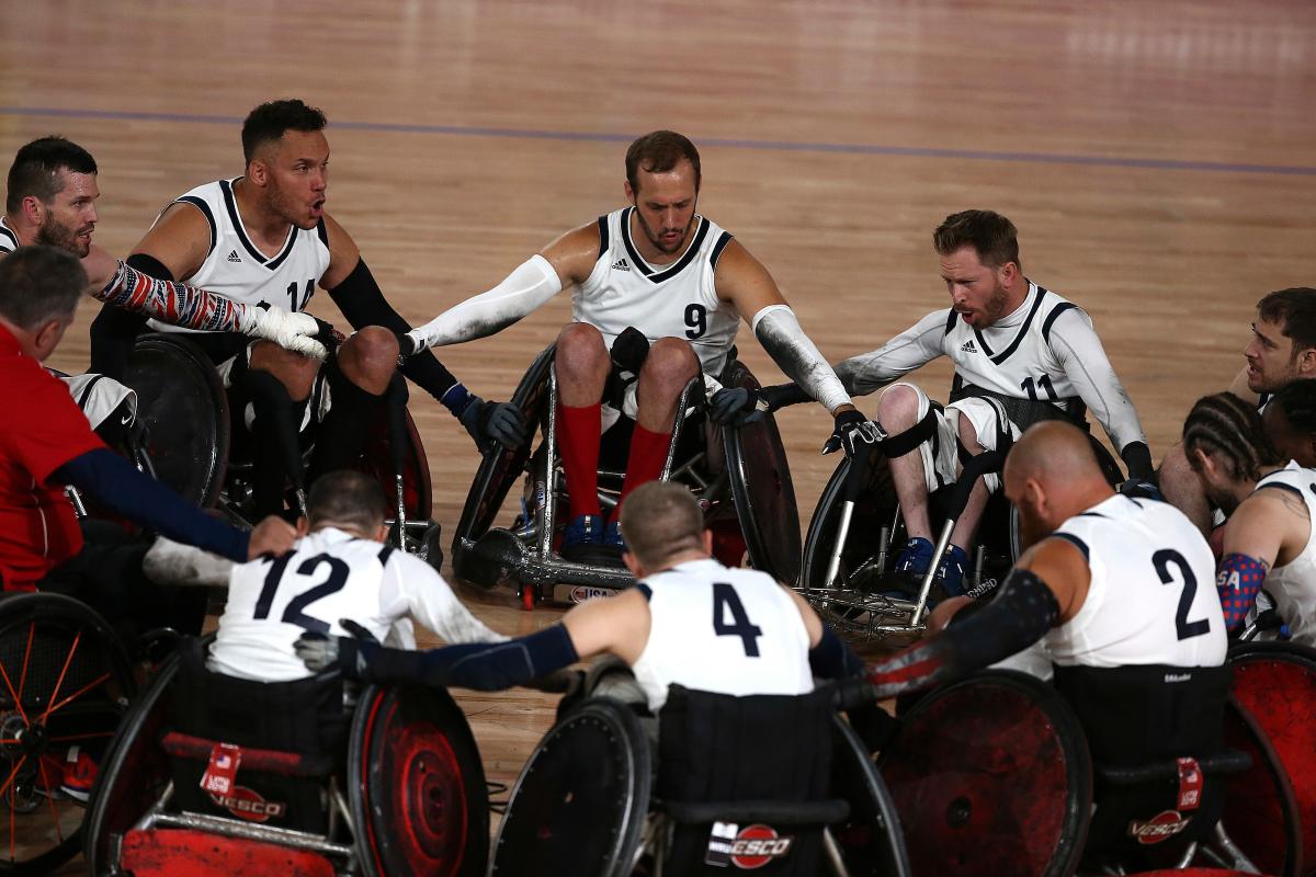 a group of male wheelchair rugby players in a circle holding arms