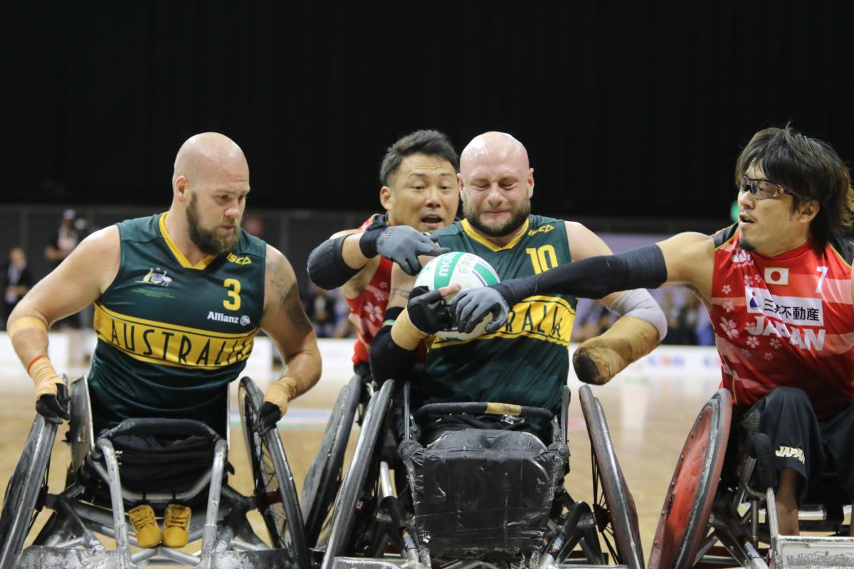 Man tries to hold onto wheelchair rugby ball while defenders surround him