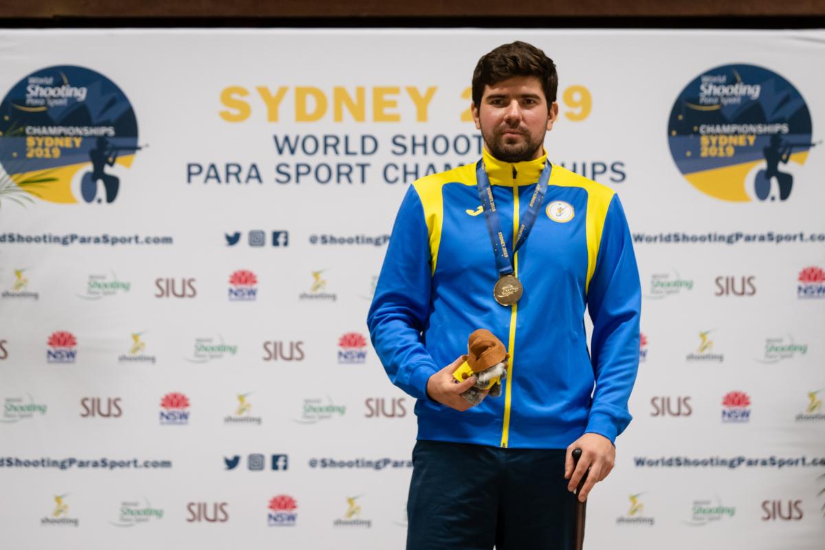 Ukrainian man stands with gold medal around neck and prize in hand