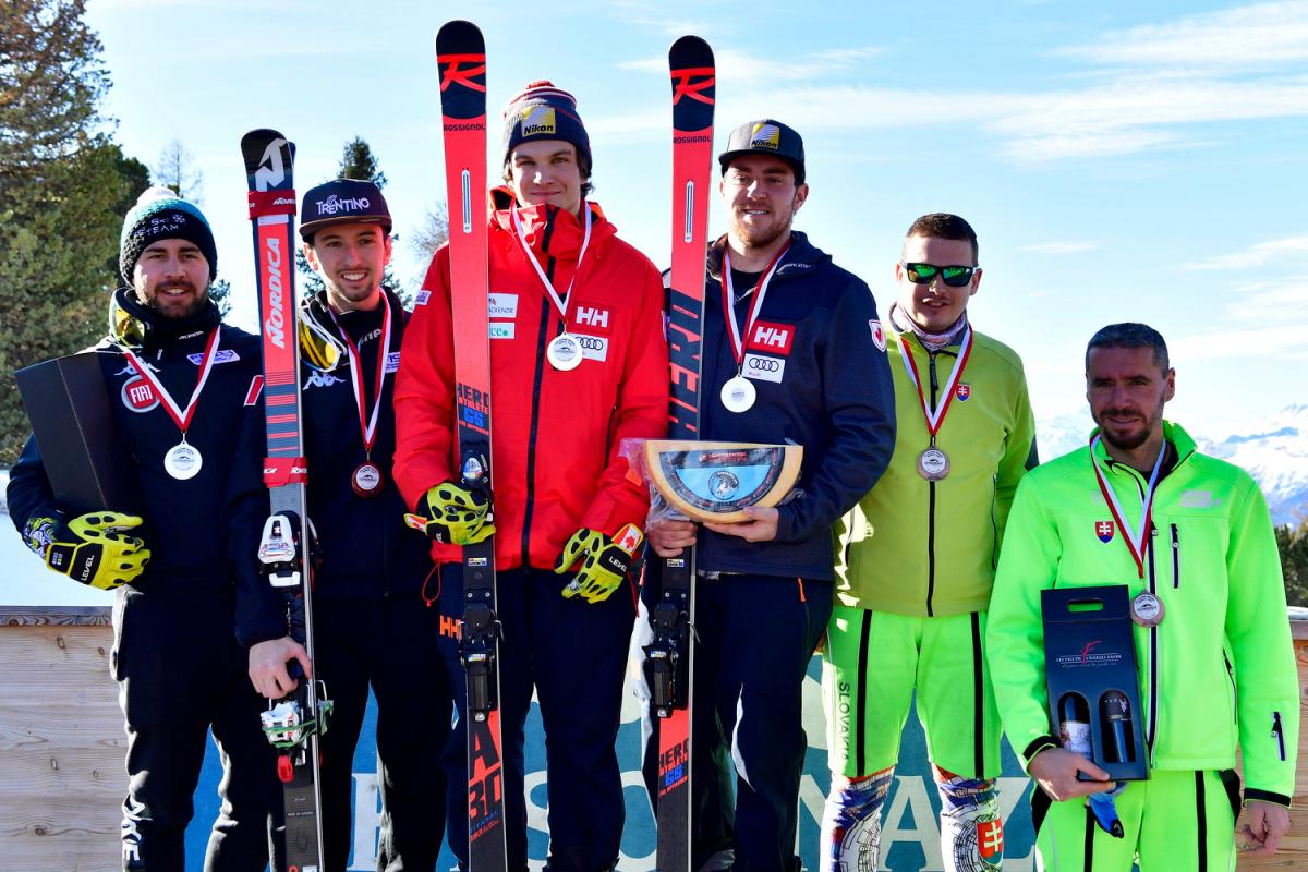 Three vision impaired male skiers with their guides pose on a podium