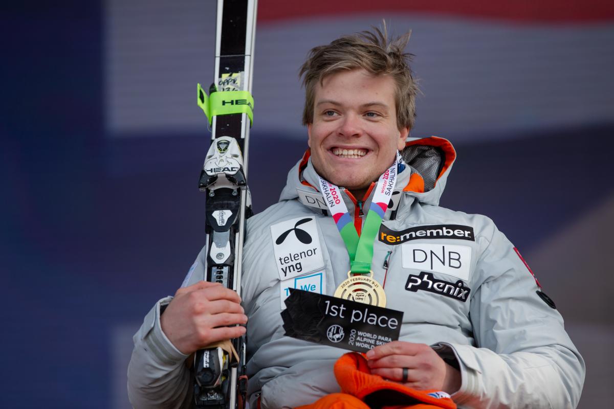 A man with a gold medal smiling and holding a skiing