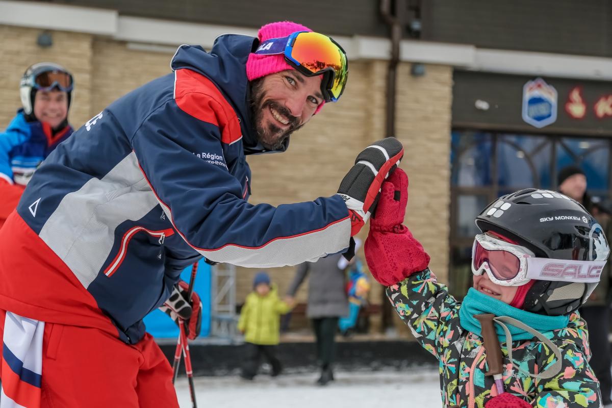 A male Para alpine skier giving a high-five to a little girl in alpine skiing outfit