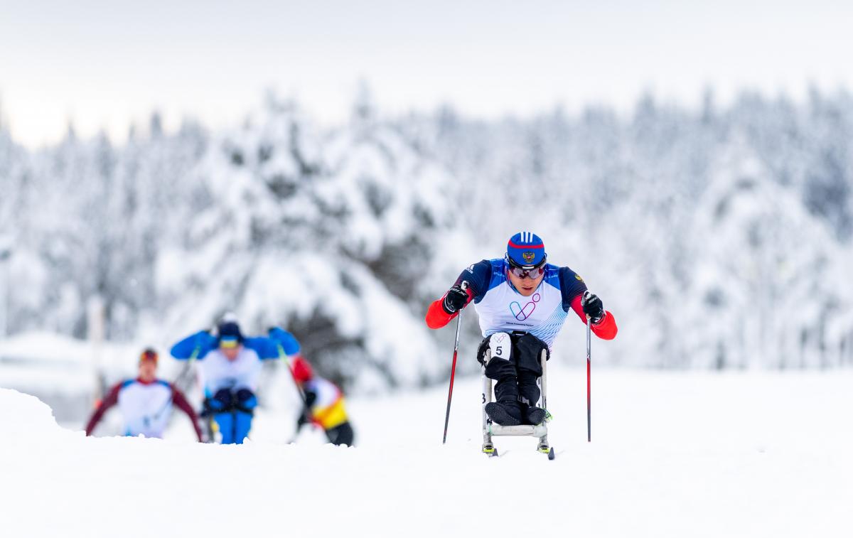A male sit-skier competing in Para cross-country followed by three competitors