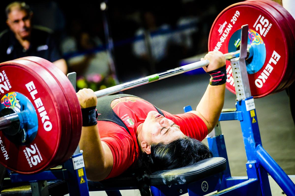 A female powerlifter competing being observed by a man in a chair