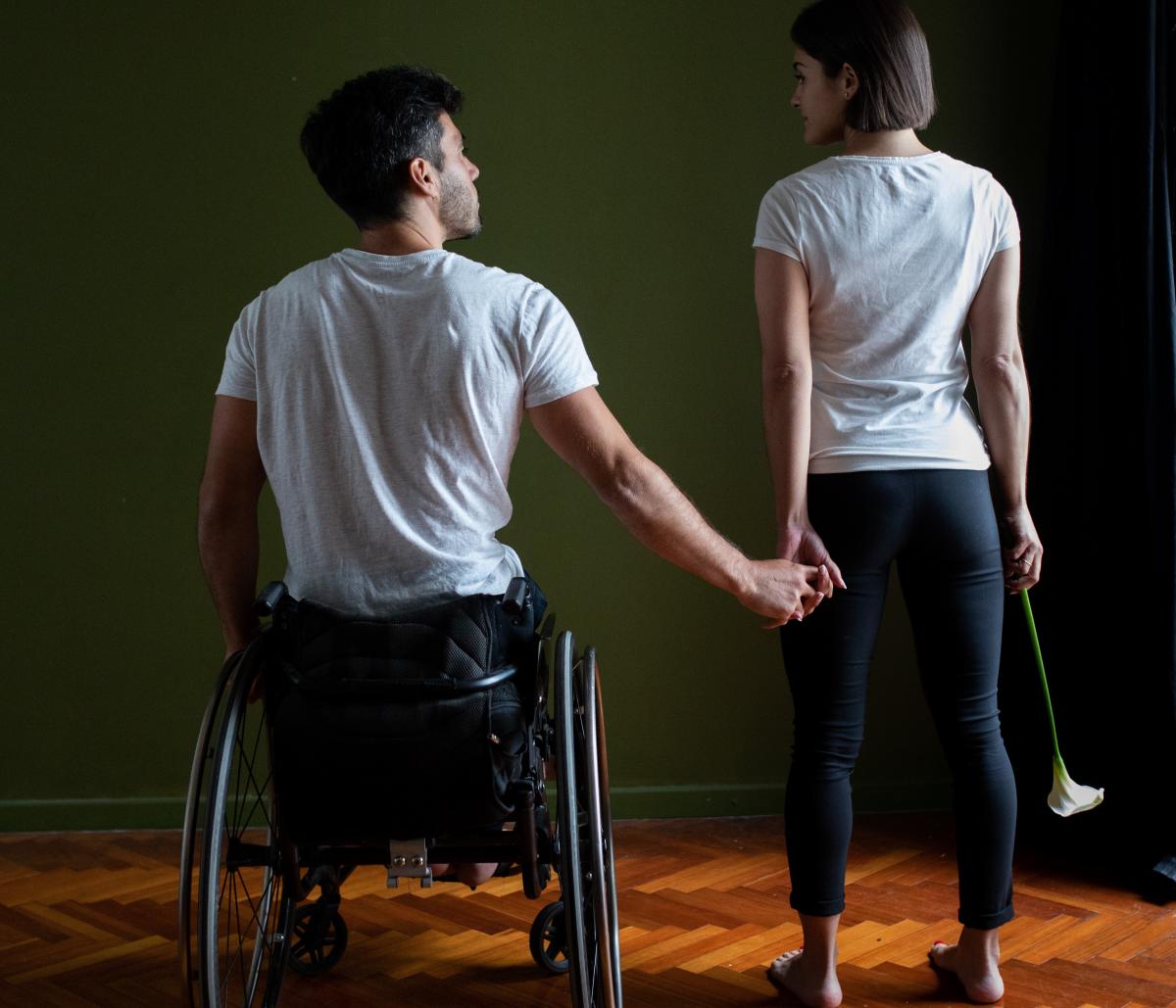 A man in a wheelchair holding the hand of a standing woman