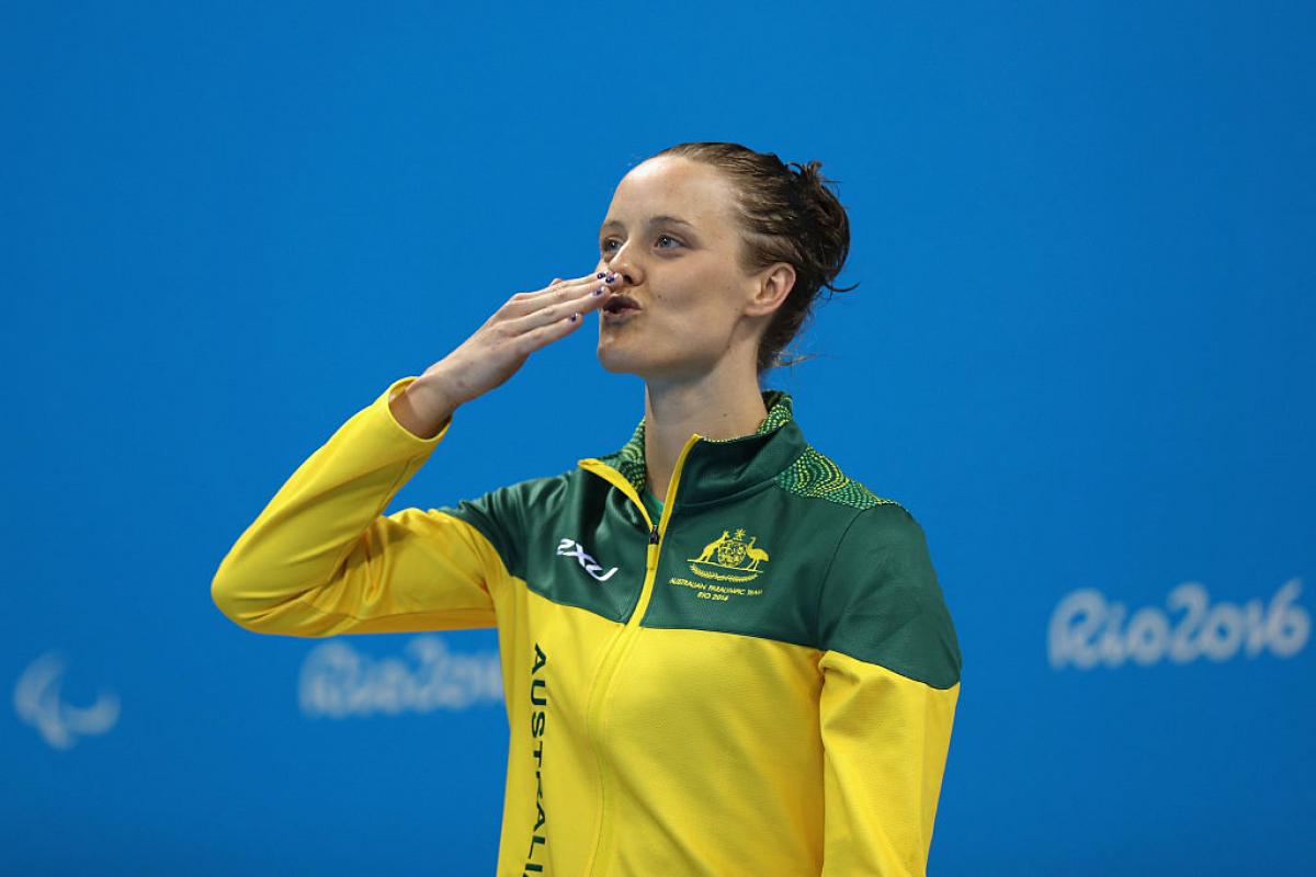 A woman sending a kiss to the audience while standing on the podium waiting to receive a medal