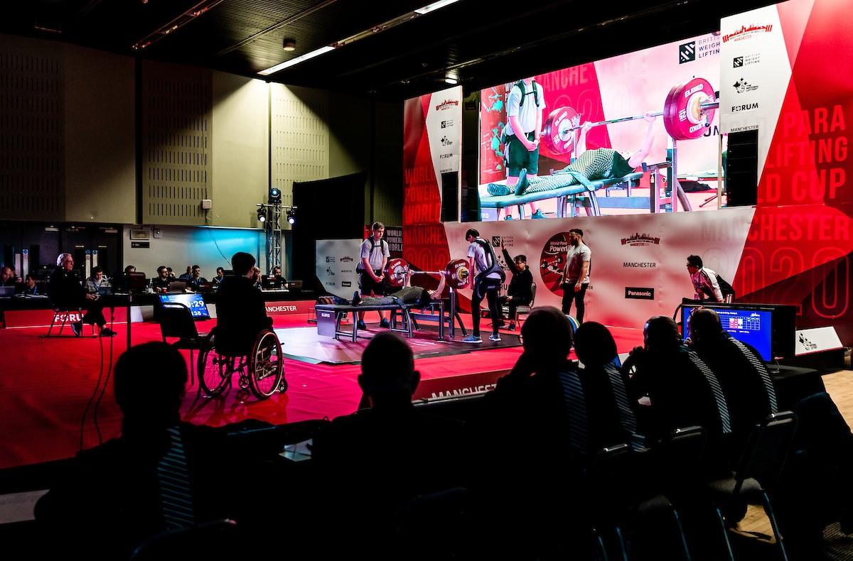 A group of people watching the stage of a Para powerlifting competition with a person competing surrounded by five people