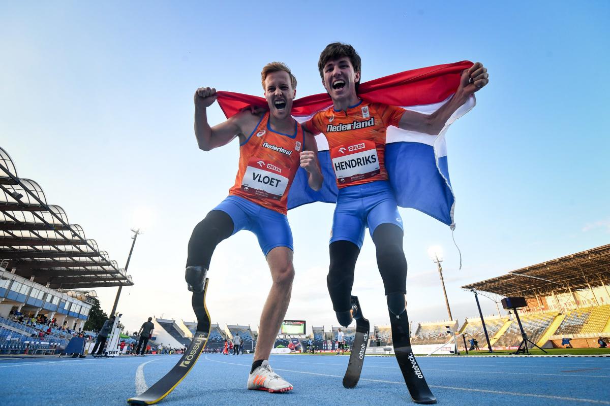 Two male sprinters with prosthetic legs celebrating with the flag of Netherlands