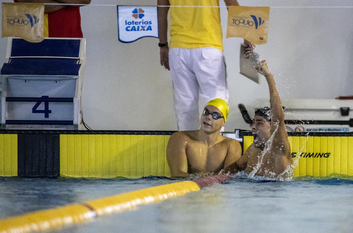 A male swimmer celebrating in the swimming pool next to another male swimmer