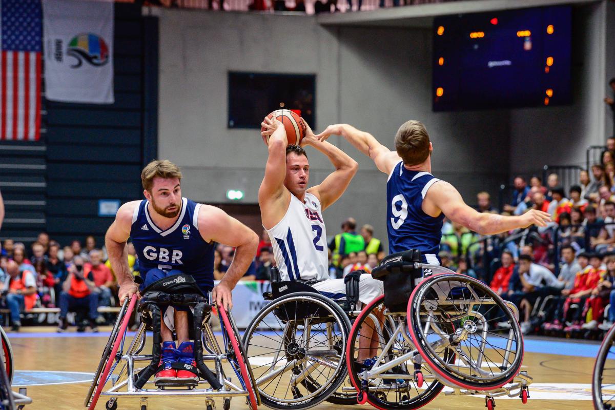 US wheelchair basketball player Jake Williams holds the ball on top of his head preventing British defenders from taking posession of it