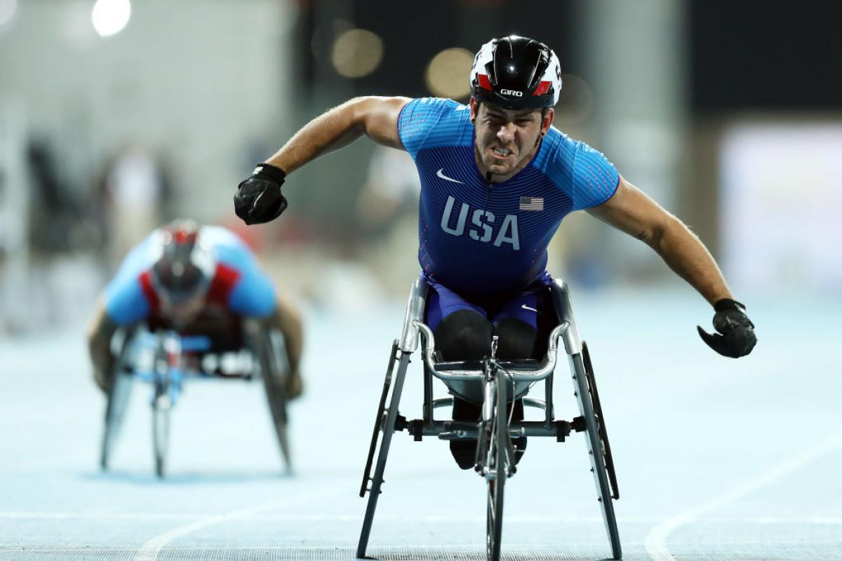 A man in a racing wheelchair celebrating with another competitor in the background