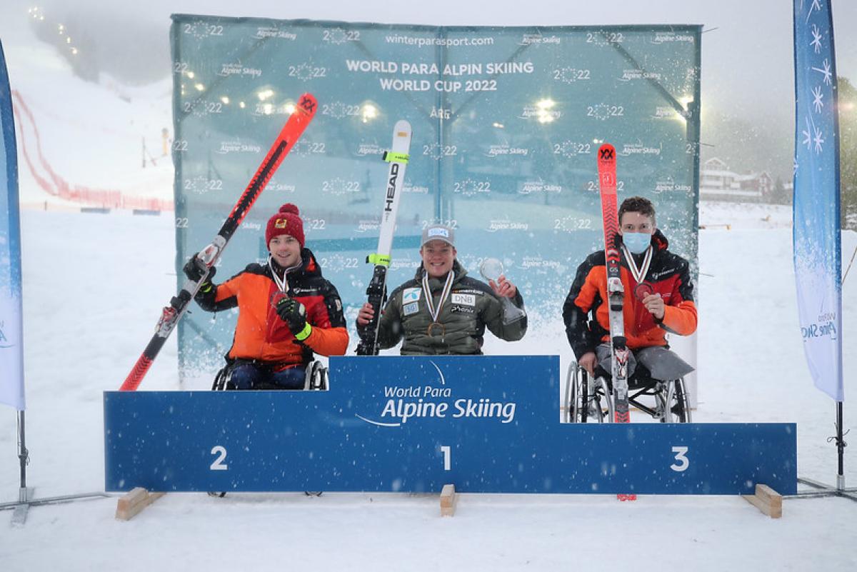 Three men in wheelchairs holding skis in a medal ceremony in the snow
