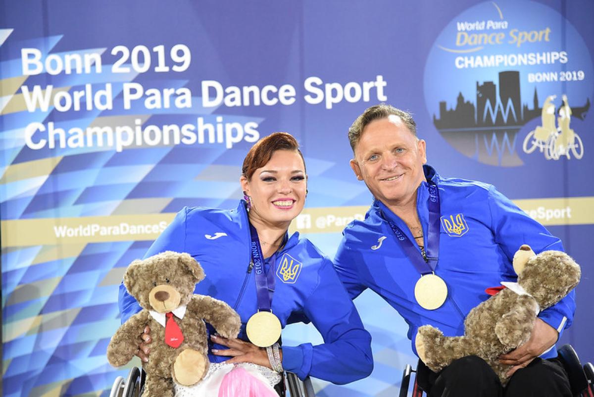 Image of a male and a female dancer in their wheelchairs and with their gold medals
