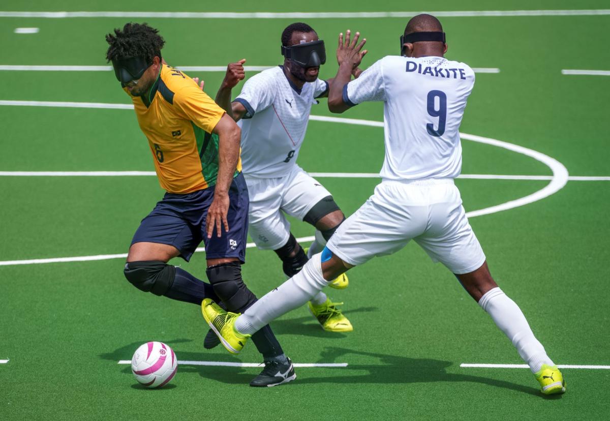 A Brazilian player breaks through a tackle from two French players in a blind football match at Tokyo 2020.