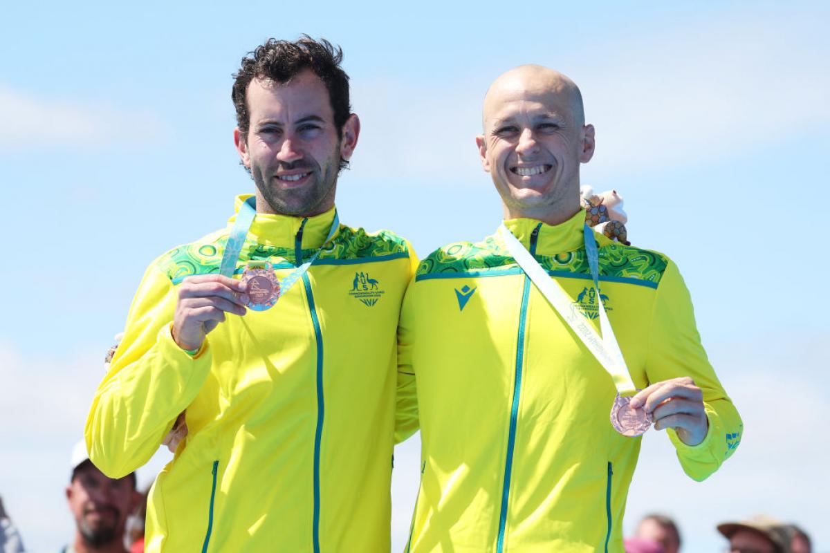 Para triathlete and his guide each hold a bronze medal and smile