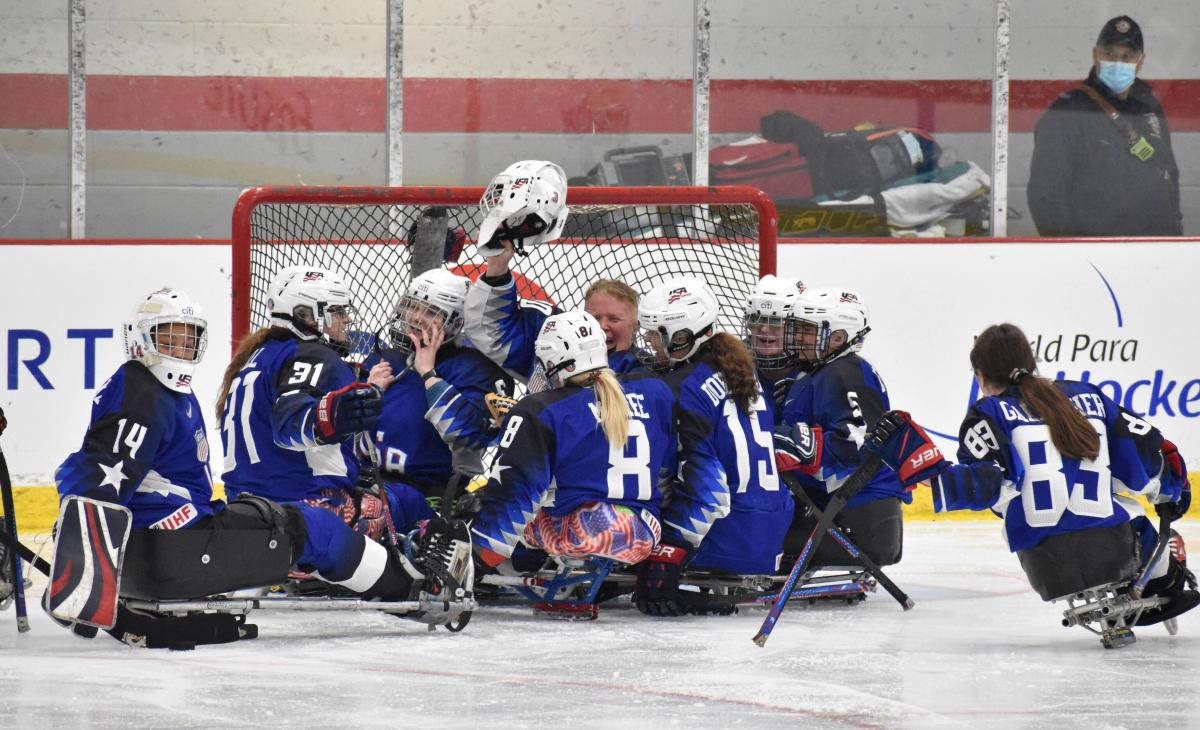 Female Para ice hockey players on sleds celebrate in a circle.