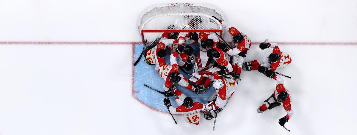 An aerial view of a Para ice hockey team celebrating in front of the goal on an ice rink