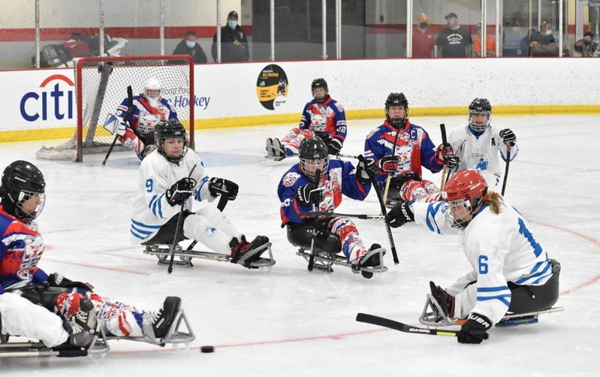 Seven female Para ice hockey players on ice in front of a goalie