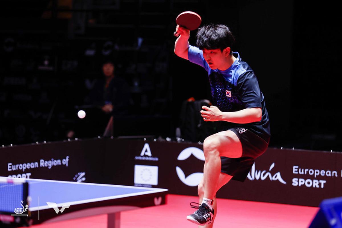 A male table tennis player jumps backward with a table tennis racket in his right hand