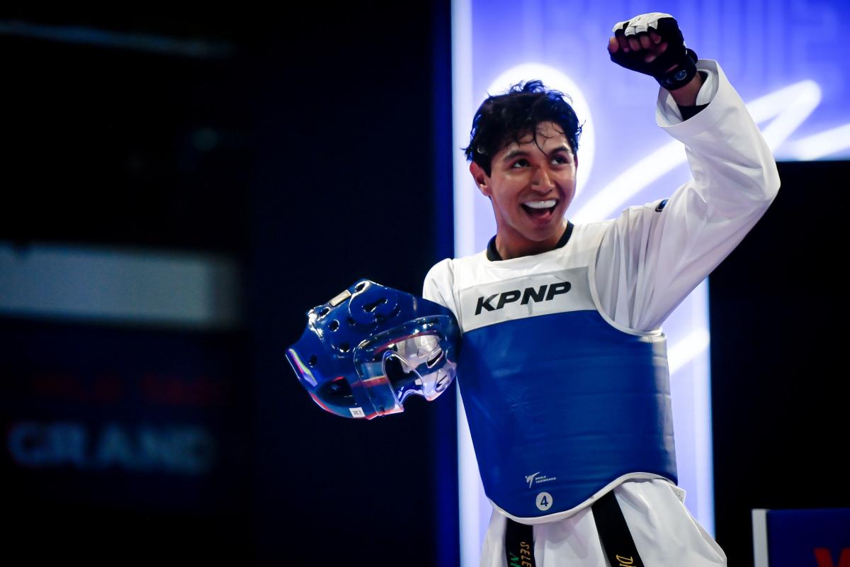 A male Para taekwondo athlete pumps his fist with his helmet off.