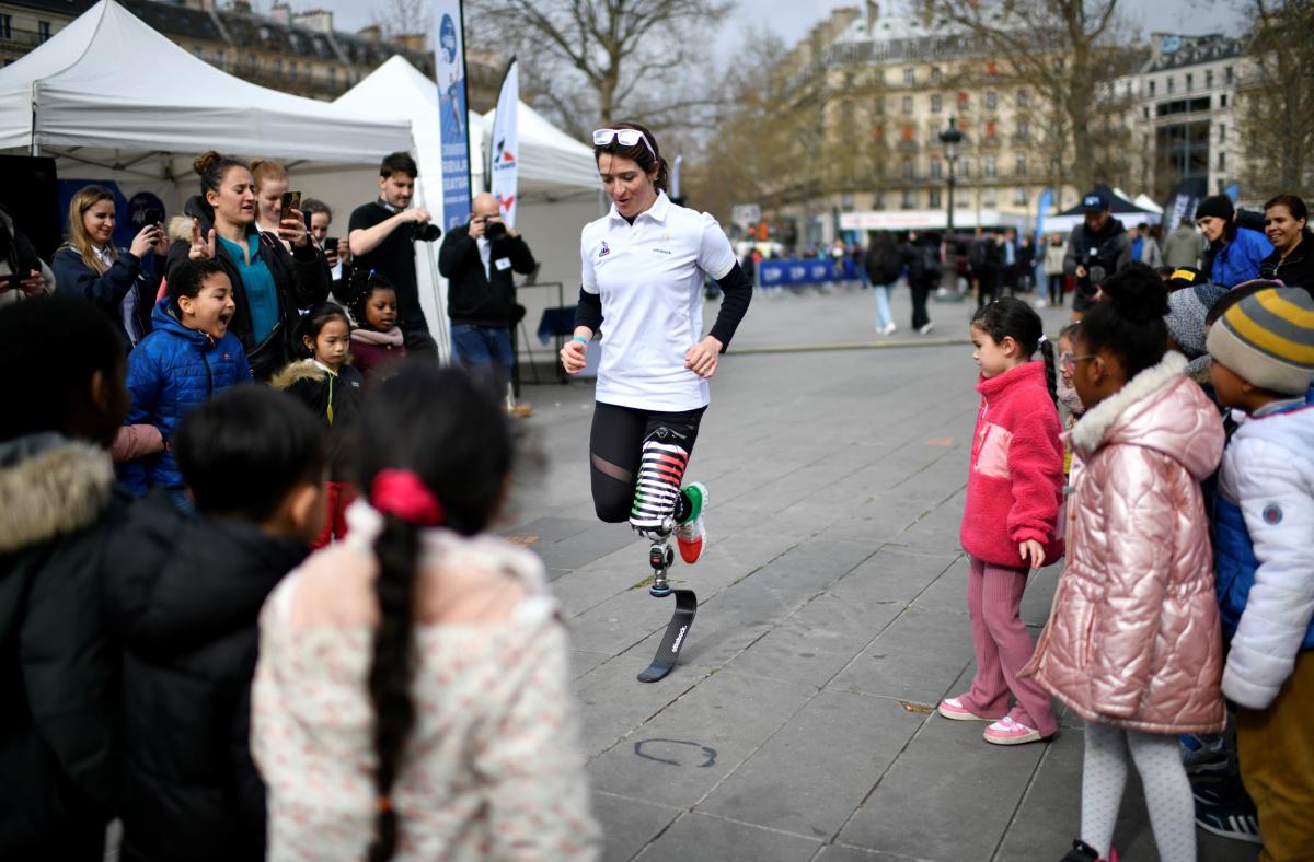 A woman with a prosthetic leg running in a square in the middle of a group of children and adults