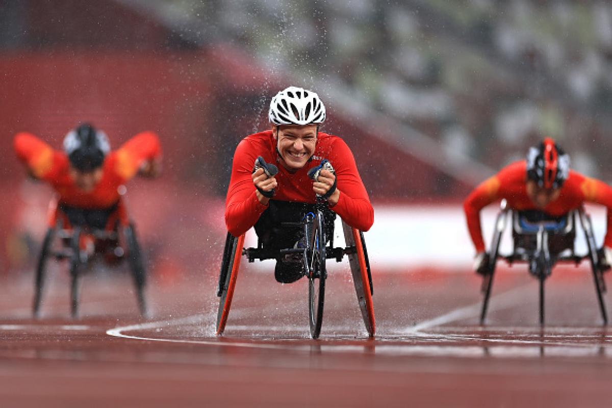 A female wheelchair racer celebrating ahead of two other racers