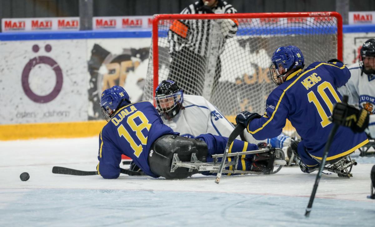 Two Swedish players in front of the Finnish goaltender in a Para ice hockey game