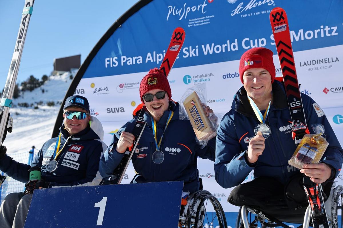 Three male sit skiers pose for a photo on the podium.