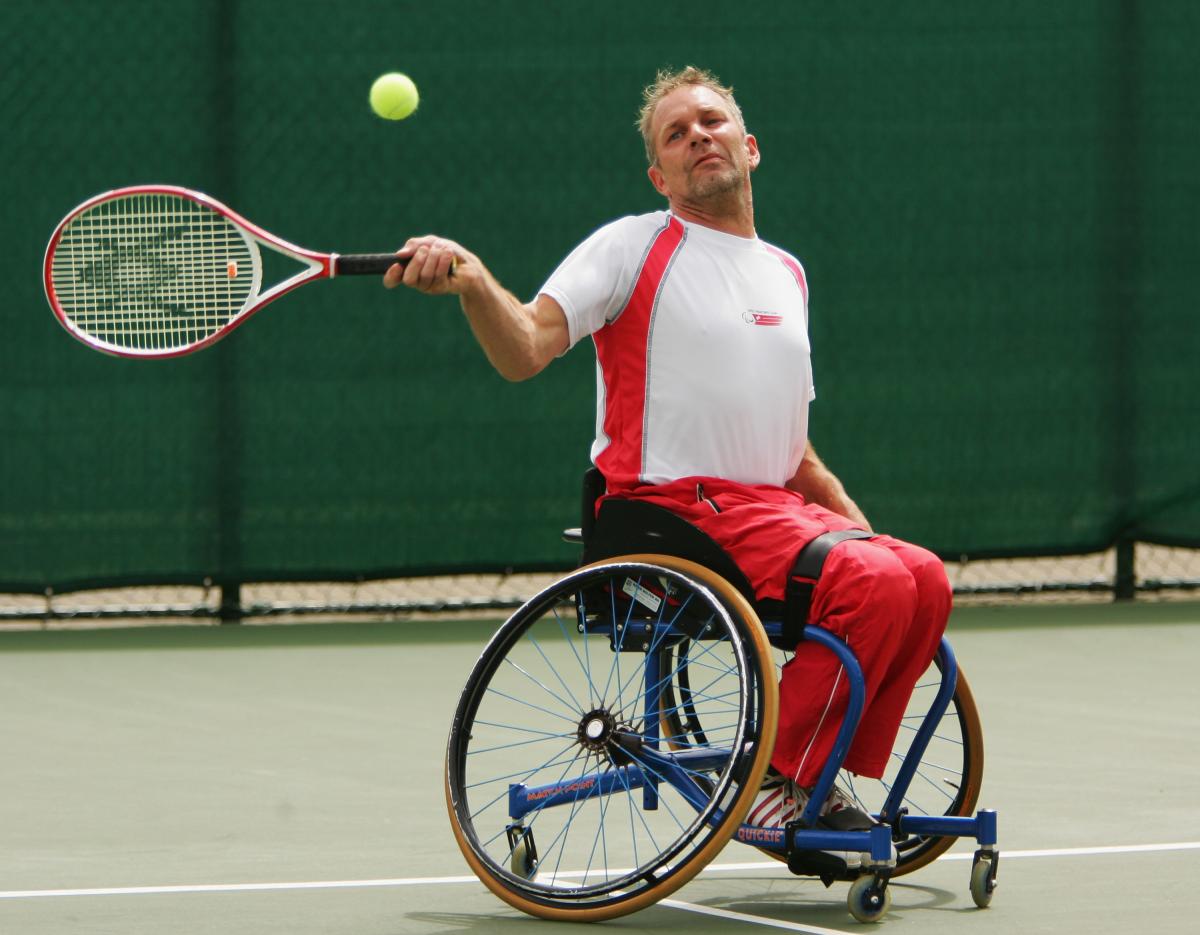 A picture of a man in a wheelchair playing a forehand in a tennis match