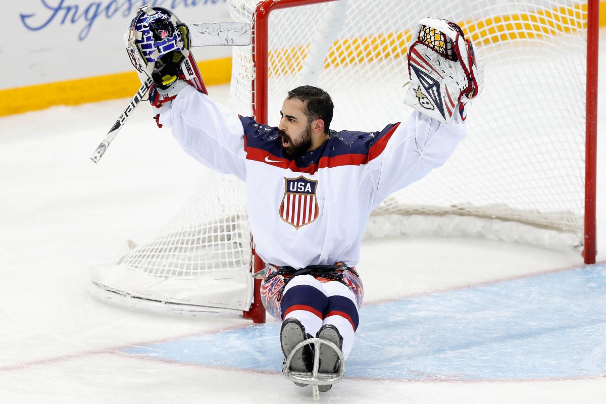 An ice sledge hockey goaltender raises his arms in celebration.