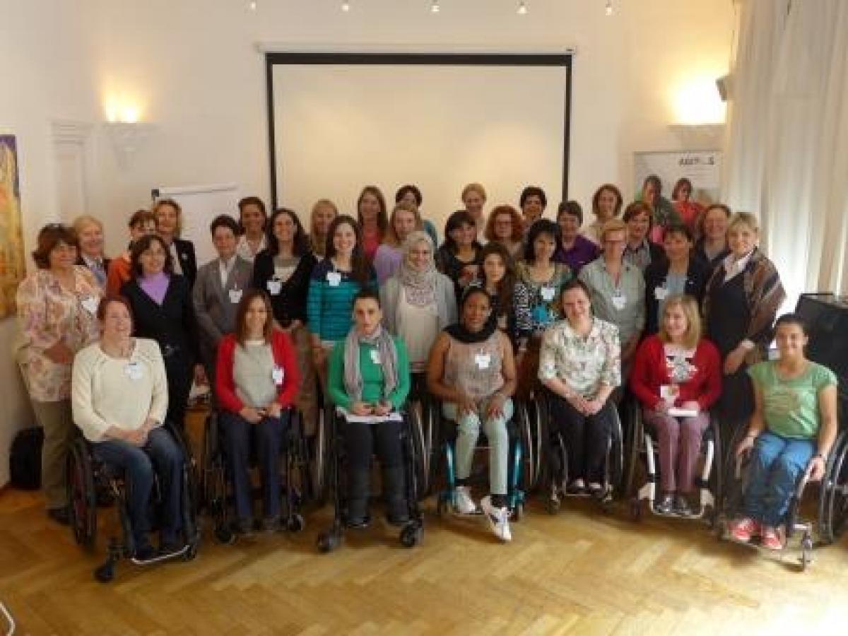 Group shot of women (standing and in wheelchairs) in front of a white wall.