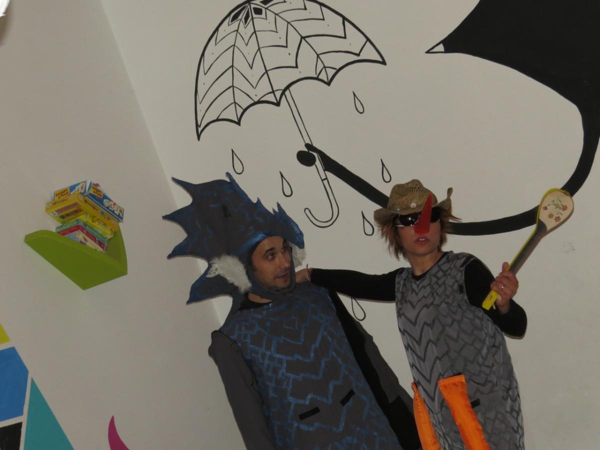 Two persons with a dragon costume stand in front of a wall. An umbrella is painted on the wall behind.