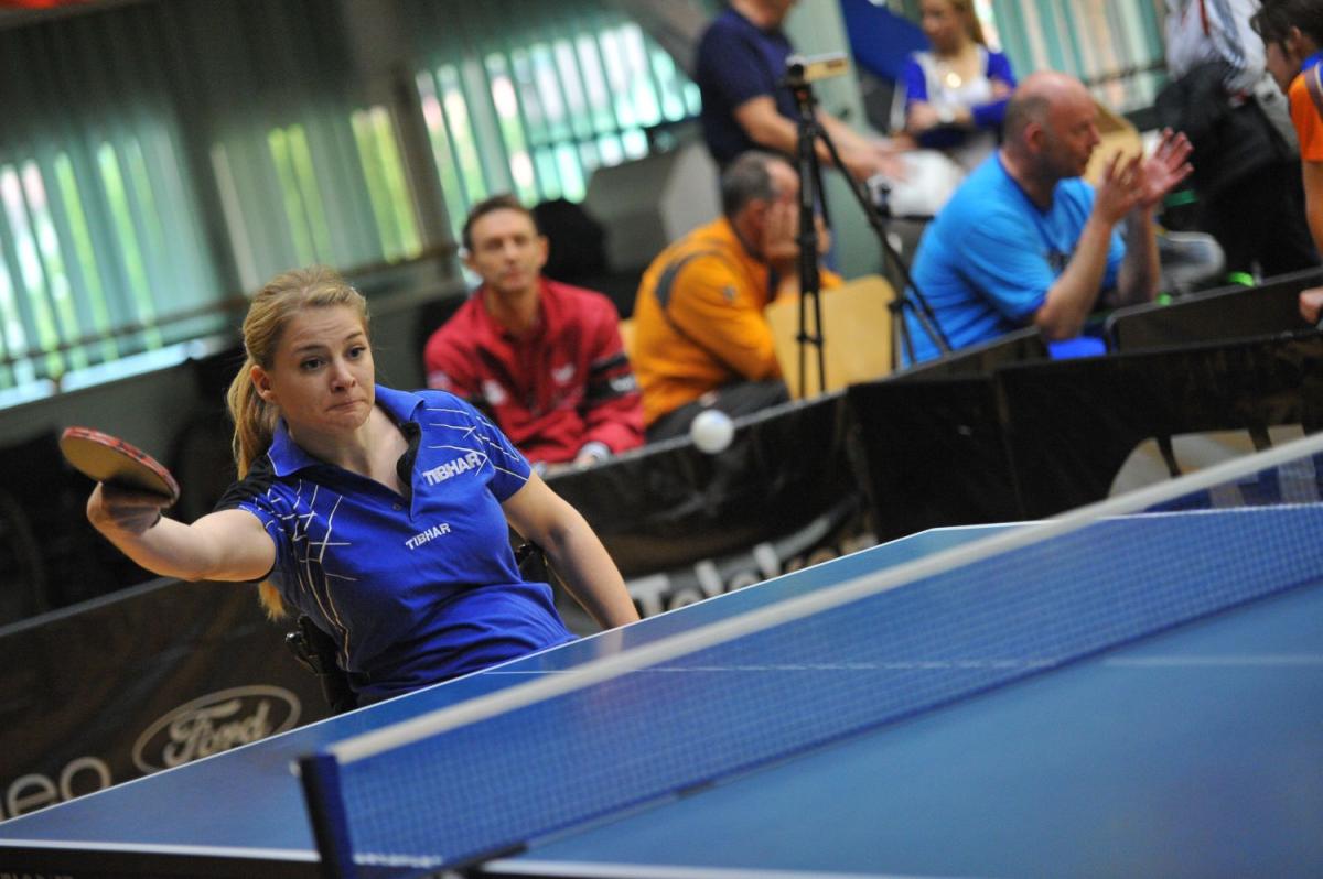 Women in wheelchair in behind a table tennis table batting the ball.