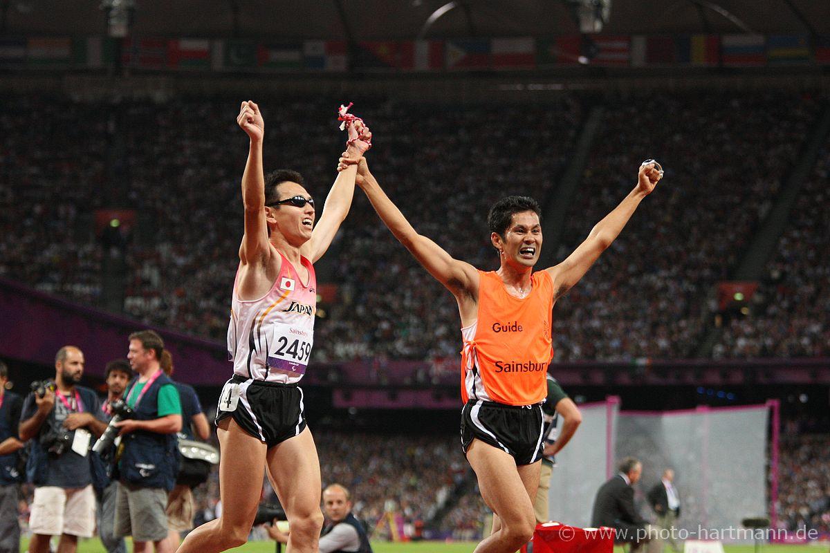 Runner with a guide crossing the finish line with their hands in the air